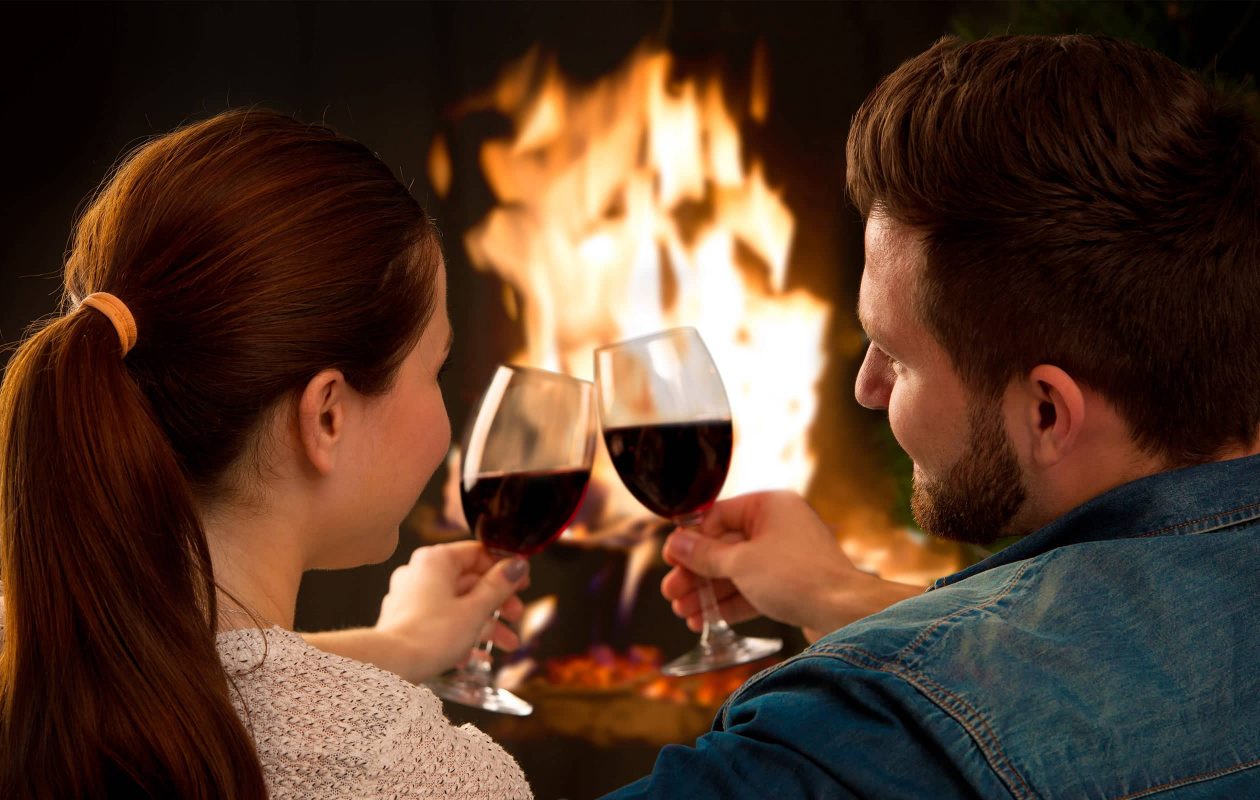 Couple toasting red wine in front of fireplace