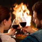 Couple toasting red wine in front of fireplace